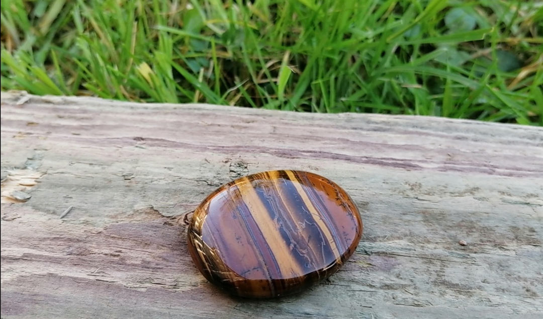 kamień naturalny tygrysie oko na starej desce na trawie